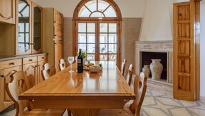 Un comedor con mesa de madera, sillas, chimenea y un amplio ventanal de arco.