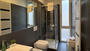A modern bathroom with a glass-enclosed shower, a toilet, a sink with a mirror, and a towel rack. - The Little Beauty Studio (Pisa)