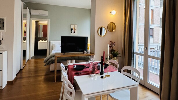 A hotel room with a dining area, a TV, and a large window with curtains. - The Little Beauty Studio (Pisa)