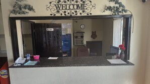 Un comptoir d’accueil avec une pancarte « Bienvenue », une horloge et un écran d’ordinateur.