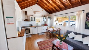 Une cuisine de taille réduite avec des meubles blancs, un coin repas comprenant une table et des chaises, et un salon avec un canapé et une plante.