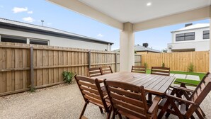 Eine Terrasse mit Holztisch und -stühlen, umgeben von einem Holzzaun und einer Rasenfläche.