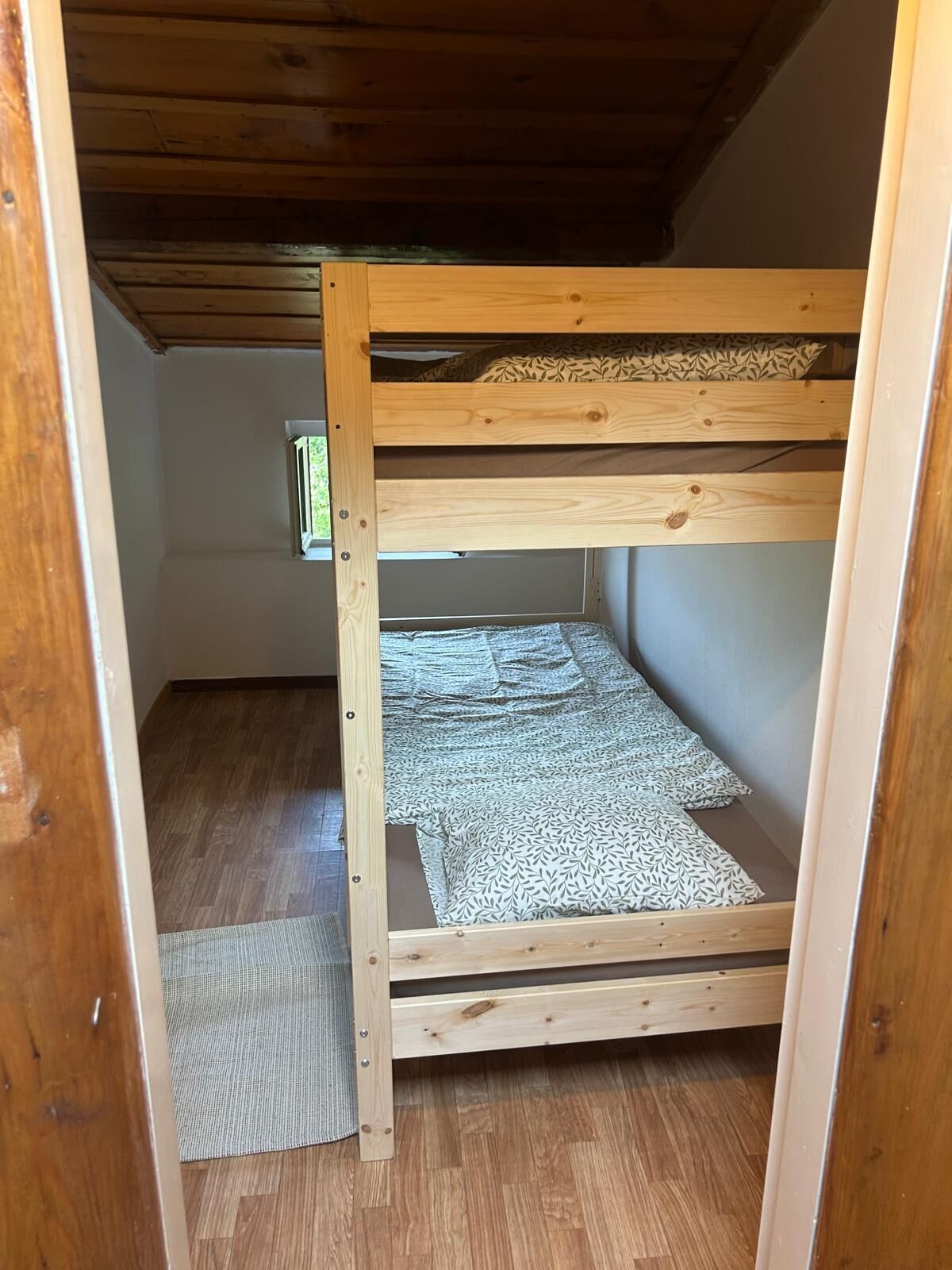 A bunk bed with a wooden frame, a mattress with a leaf pattern, and a woven mat at the foot of the bed.