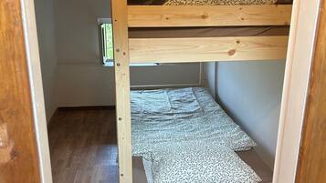A bunk bed with a wooden frame, a mattress with a leaf pattern, and a woven mat at the foot of the bed.