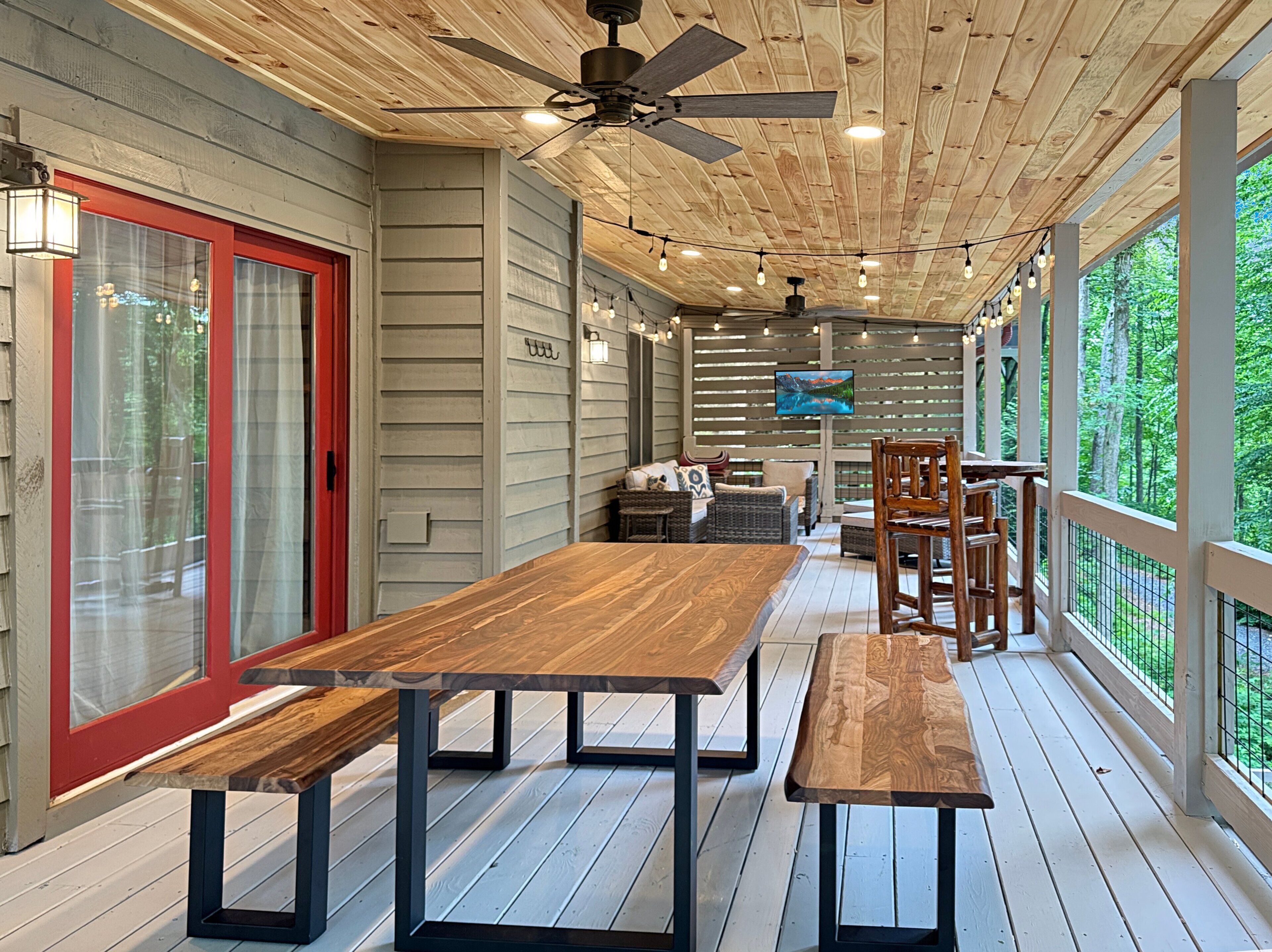 A wooden deck with a dining table and benches, a ceiling fan, and a TV mounted on the wall.