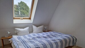 Makuuhuone, jossa on kalteva katto, raidallinen peitto sängyllä, kaksi yöpöytävalaisinta ja ikkuna, josta avautuu näkymä puihin.