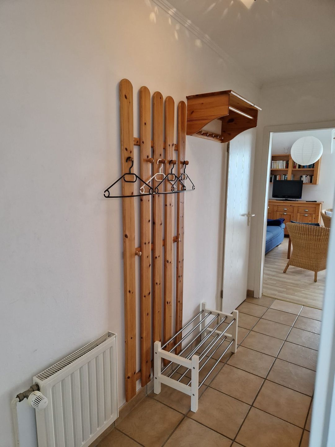 A hallway with a ski rack, a radiator, and a wicker chair.