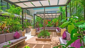 A covered outdoor seating area with sofas and planters, surrounded by lush greenery. - Premium Downtown PH +Private Pool +Gym+PKG+Rooftop (Playa del Carmen)
