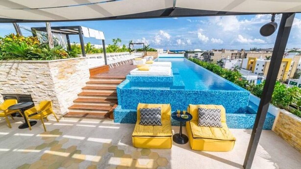 A rooftop pool area with yellow chairs and a stone wall. - Premium Downtown PH +Private Pool +Gym+PKG+Rooftop (Playa del Carmen)