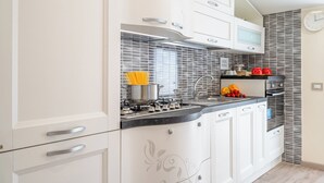 Une cuisine moderne avec des meubles blancs, une cuisinière à gaz et un évier en acier inoxydable.