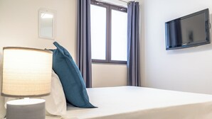Une chambre d’hôtel avec un lit, une lampe de chevet, un téléviseur fixé au mur et une fenêtre avec des rideaux.