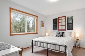 Een slaapkamer met een groot raam, een bed met metalen frame, een nachtkastje en een kleine lamp.