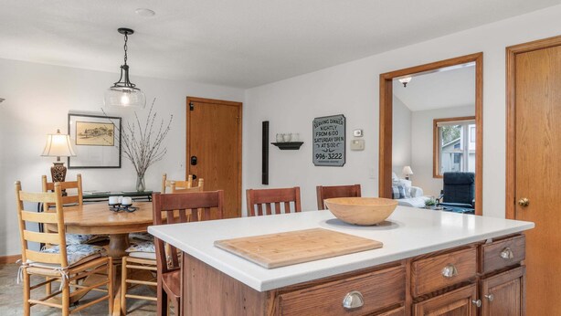A kitchen with a wooden island, a dining table with chairs, a hanging light fixture, and a framed picture on the wall.