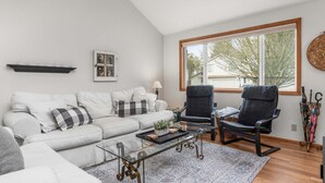 A living room with a sofa, two chairs, a coffee table, a window with a view, a wall-mounted shelf, and a wall-mounted lamp.