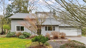 A two-story house with a garage, surrounded by a well-maintained garden with various shrubs and a lawn.