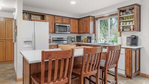 A kitchen with wooden cabinets, a white refrigerator, a microwave, a stove, and a bar area with stools.