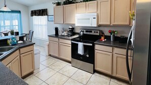 A modern kitchen with light wood cabinets, a stainless steel refrigerator, a black stove, and a skylight.