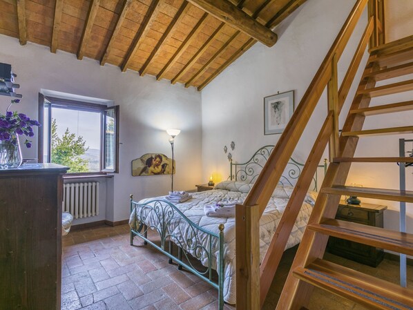 A bedroom with a wooden ceiling, a bed with a metal frame, a window with a view, and a staircase.