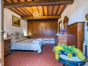 Ein Schlafzimmer mit Holzboden, einem Bett mit floralem Überwurf, einem Schminktisch, einem Spiegel und einer Zimmerpflanze.