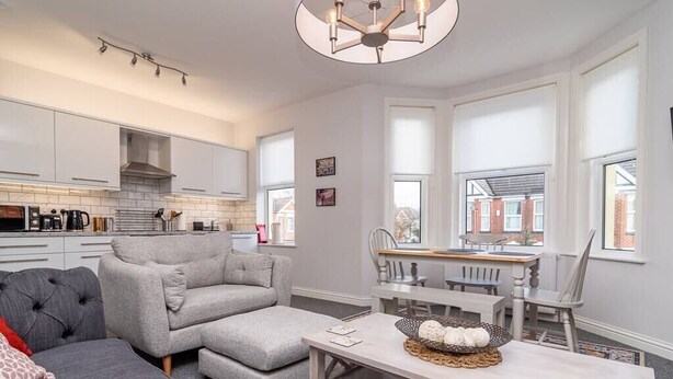 Een moderne keuken met witte kasten, een grijze bank en een eethoek met een houten tafel en stoelen.