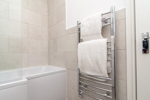 A modern bathroom with a white bathtub, a towel rack with two towels, and beige tiled walls. - (Boscombe)