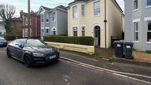 Een woonstraat met huizen, een geparkeerde auto en een haag.