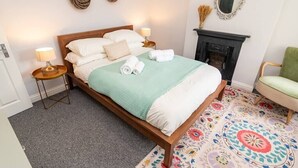 Een keurig opgemaakt slaapkamer met een bed, bedlampjes, een openhaard en een kamerbreed tapijt.