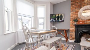 Een eetgedeelte met een houten tafel en stoelen, een aan de muur bevestigde televisie en een schouw van baksteen.