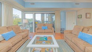 A living room with two beige sofas, a glass coffee table, and a view through a sliding glass door to an outdoor area. - Oceanfront Ocean Club Villa in Wild Dunes w/Hot Tub & Community Pool! *Unit 1212* (Isle Of Palms)