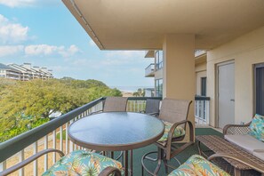 A balcony with a round table and chairs, overlooking a beach and a residential area.