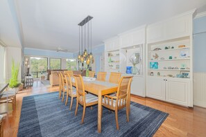 A spacious dining area with a wooden table and chairs, a blue rug, and a ceiling fan.