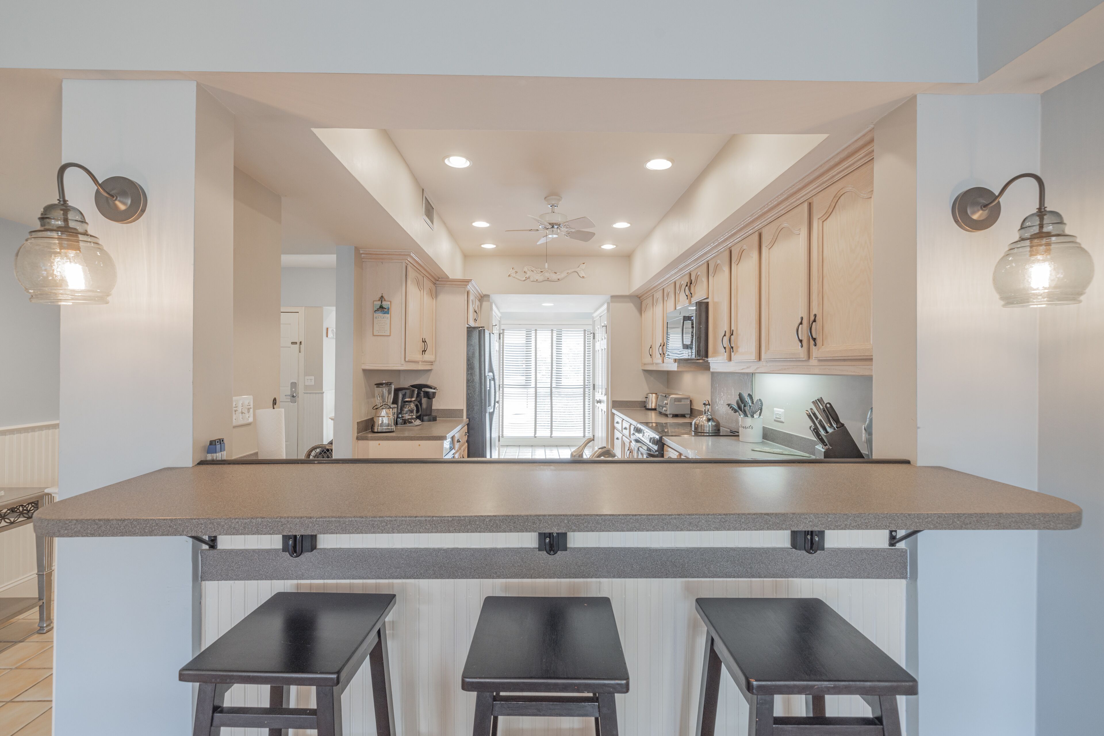 A kitchen with a central island, bar stools, wooden cabinets, and pendant lighting.
