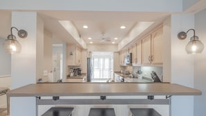 A kitchen with a central island, bar stools, wooden cabinets, and pendant lighting. - Oceanfront Ocean Club Villa in Wild Dunes w/Hot Tub & Community Pool! *Unit 1212* (Isle Of Palms)
