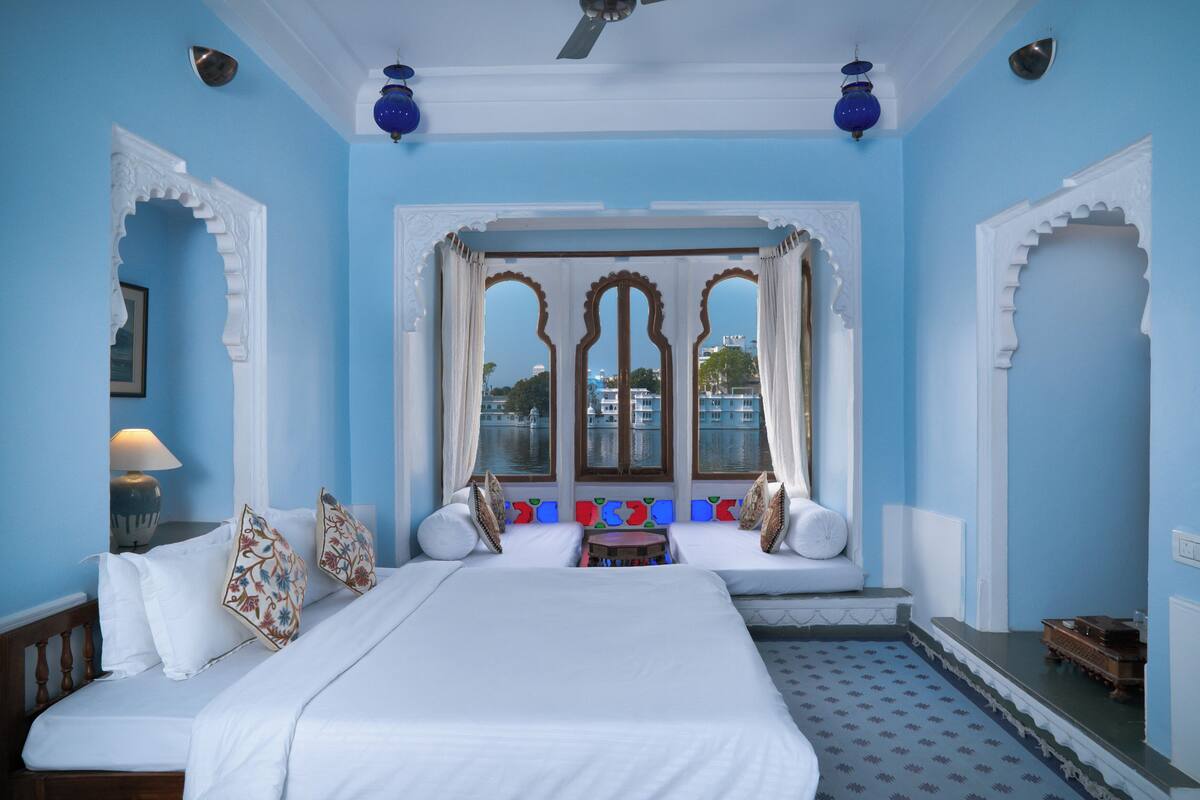 A room with a large bed, a small table, and a view through a window with decorative arches.