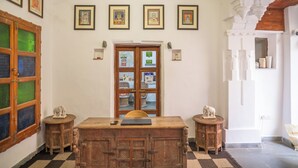 A room with a wooden desk, two small side tables, a door with glass panels, and framed pictures on the wall. - KANKARWA HAVELI (Udaipur)