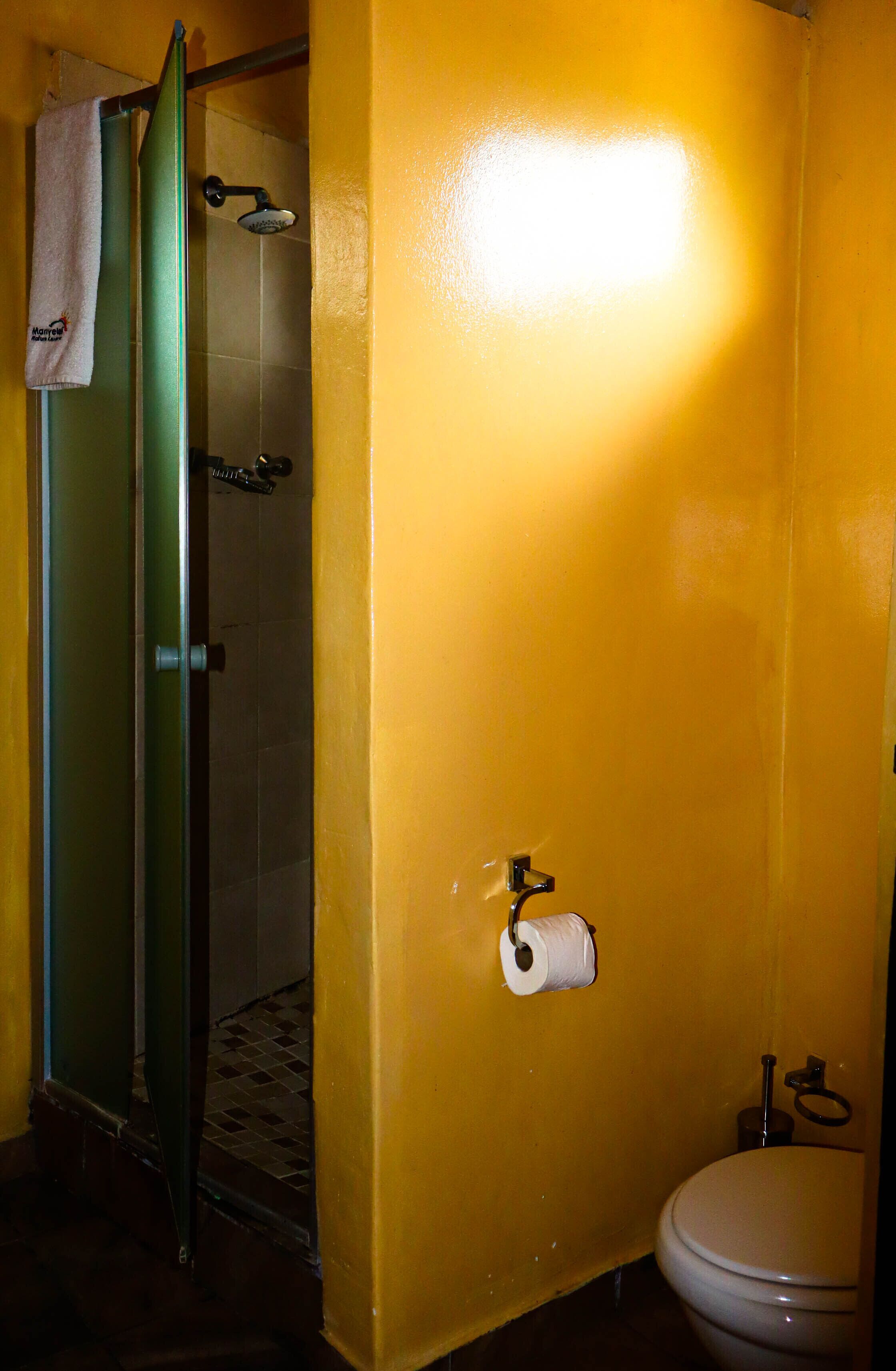 A bathroom with yellow walls, a shower, a toilet, and a towel hanging on the door.