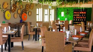 A restaurant with multiple tables and chairs, a green wall with a menu board, and a shelf with snacks. - Self Catering Chalets - Manyeleti (Manyeleti)