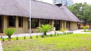 A building with a thatched roof, a paved walkway, and a well-maintained lawn with various plants. - Self Catering Chalets - Manyeleti (Manyeleti)