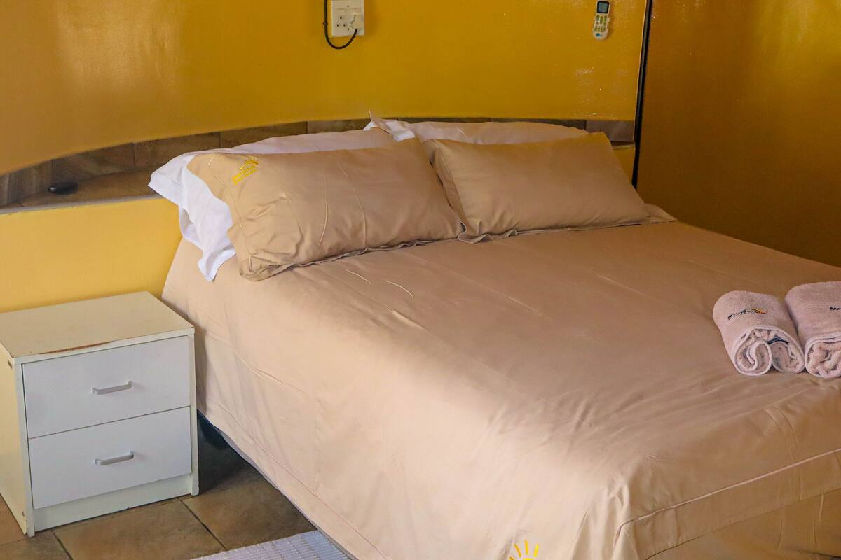 A hotel room with a bed, two pillows, a nightstand with drawers, and a pair of towels on the bed.