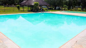 A rectangular swimming pool with a tiled deck, surrounded by grass and trees. - Self Catering Chalets - Manyeleti (Manyeleti)