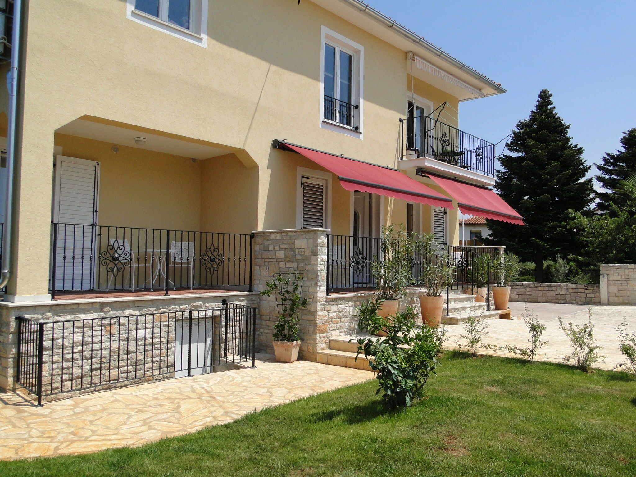 A two-story house with a stone facade, a red awning over the entrance, and a stone staircase leading to the front door.