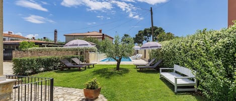 A backyard with a swimming pool, lounge chairs, and a stone pathway.