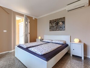 Ein Schlafzimmer mit einem Bett, zwei Nachttischen mit Lampen, einer Wand mit einem Motivationsspruch und einer Klimaanlage.