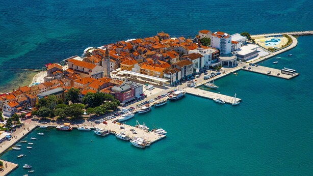 An aerial view of a coastal town with a marina, buildings with red-tiled roofs, and boats docked. - Villa Ester by Interhome (Umag)