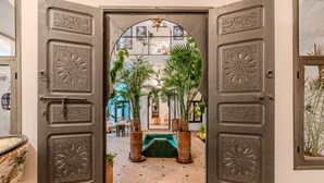 Porta aperta che dà su un cortile con piante in vaso, una piscina e vista sull'interno.
