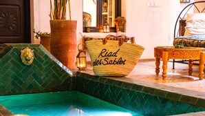 Area piscina con una borsa in tessuto etichettata "Pied des Sables" e un tavolo di legno con tovaglia fantasia.