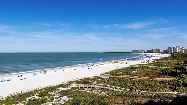 A beach with a wooden boardwalk, sandy beach, and a city skyline in the background. - Experience coastal comfort at The Somerset, your oceanfront haven on Marco Island (Marco Island)