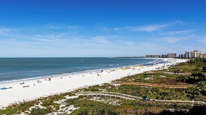 Une plage avec une promenade en bois, une étendue de sable et, en arrière-plan, la silhouette d’une ville.