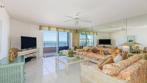 A spacious living room with a balcony, a television, and a large mirror. - Experience coastal comfort at The Somerset, your oceanfront haven on Marco Island (Marco Island)