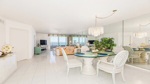 A spacious living area with a dining table, chairs, and a large window overlooking the ocean. - Experience coastal comfort at The Somerset, your oceanfront haven on Marco Island (Marco Island)